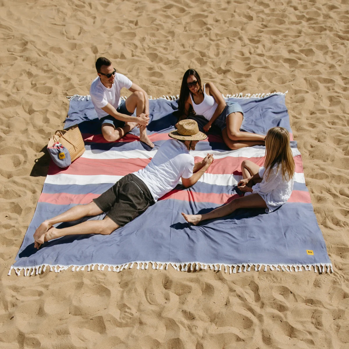 Four people relaxing on oversized blue striped beach blanket in sand