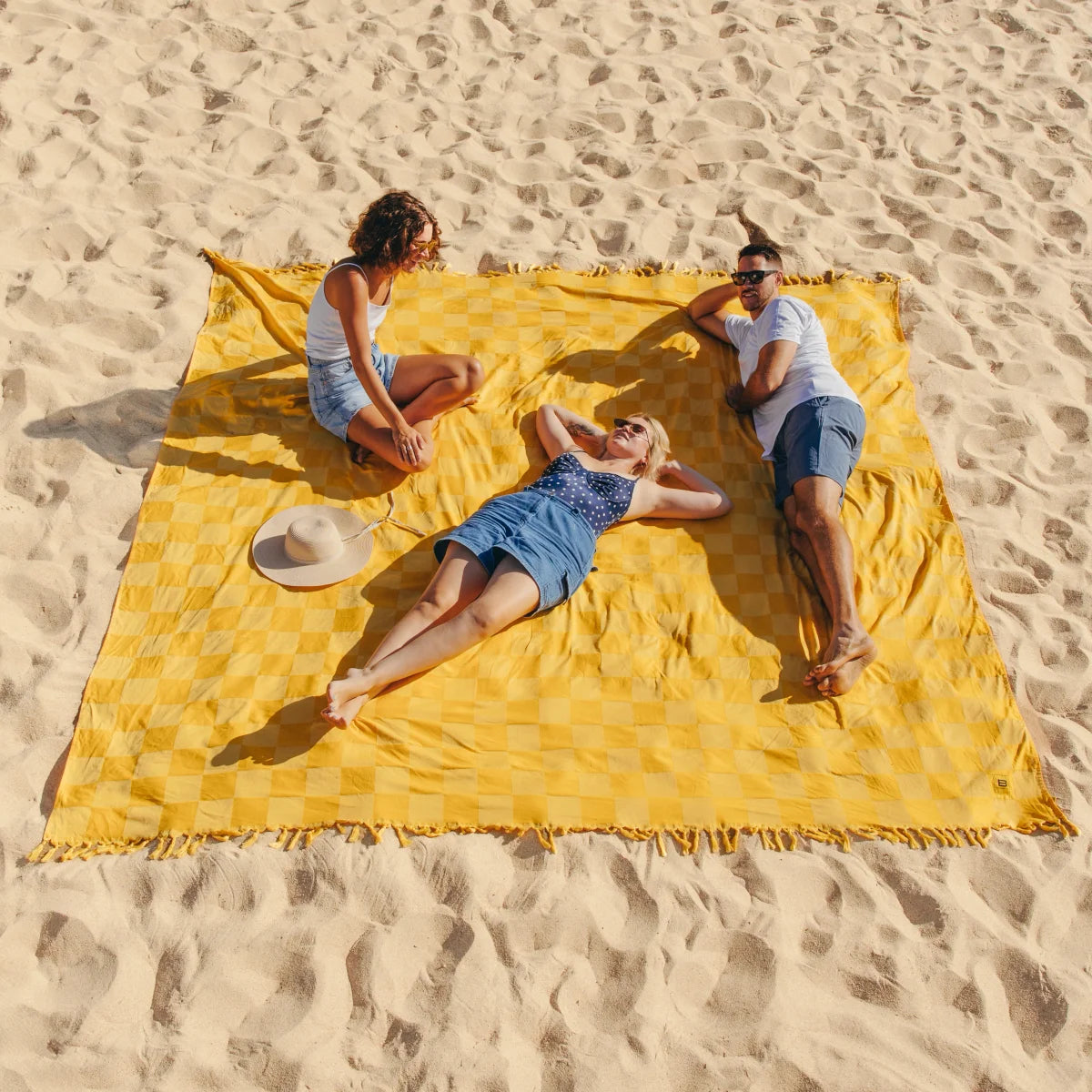 Family of three relaxing on yellow checkered oversized blanket on beach sand