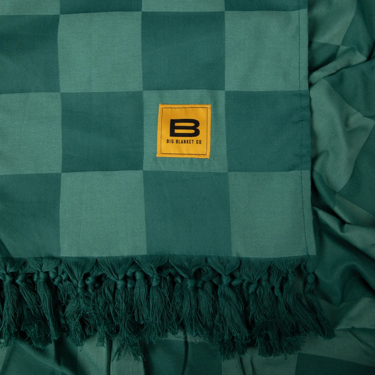 Teal and light green checkered oversized blanket with tasseled fringe trim and Big Blanket Co yellow logo tag