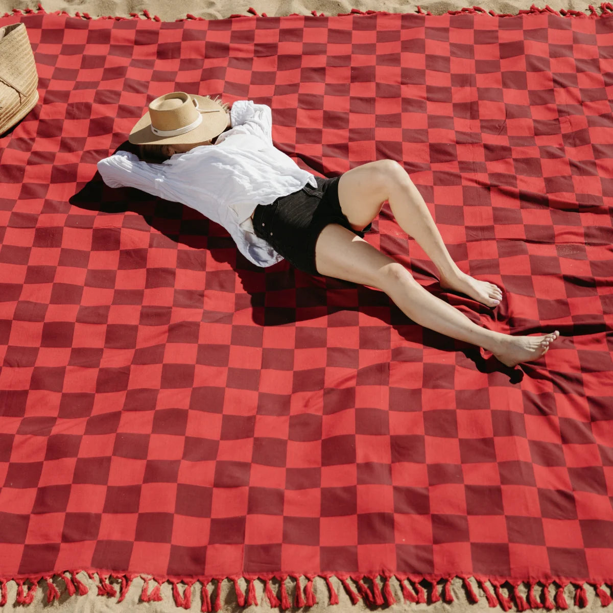Person relaxing on red checkered oversized blanket with fringed edges in outdoor setting