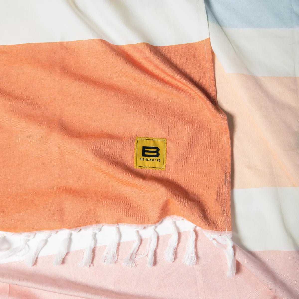 Big Beachy Blanket in Sunrise Stripes with orange, cream, and blue horizontal stripes, Big Blanket Co label visible