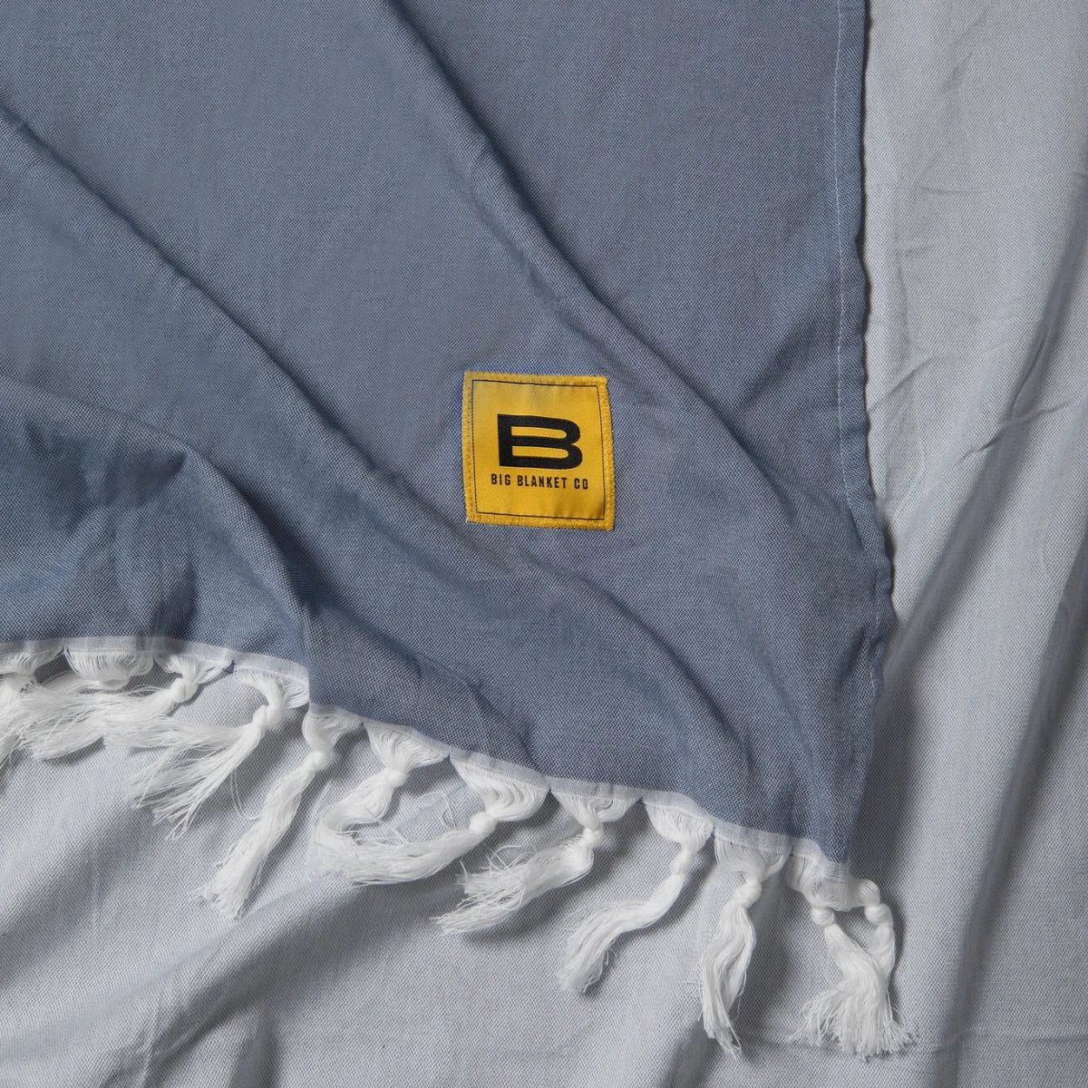Oversized slate blue blanket with white fringe trim and Big Blanket Co yellow logo label