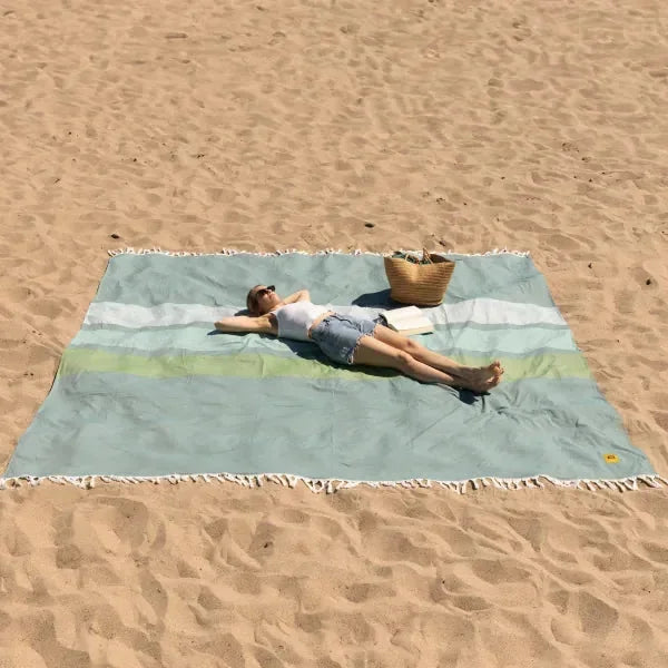 Man relaxing on oversized striped beach blanket in tidepool colors on sandy beach