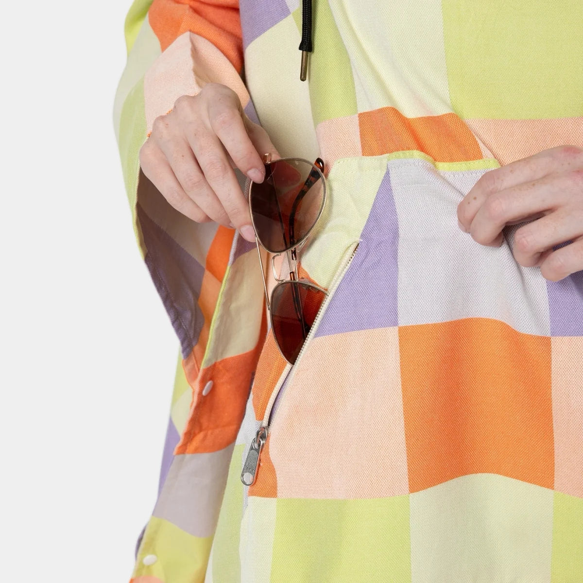 Colorful patchwork blanket poncho with orange, purple, yellow and cream squares, worn by person holding sunglasses