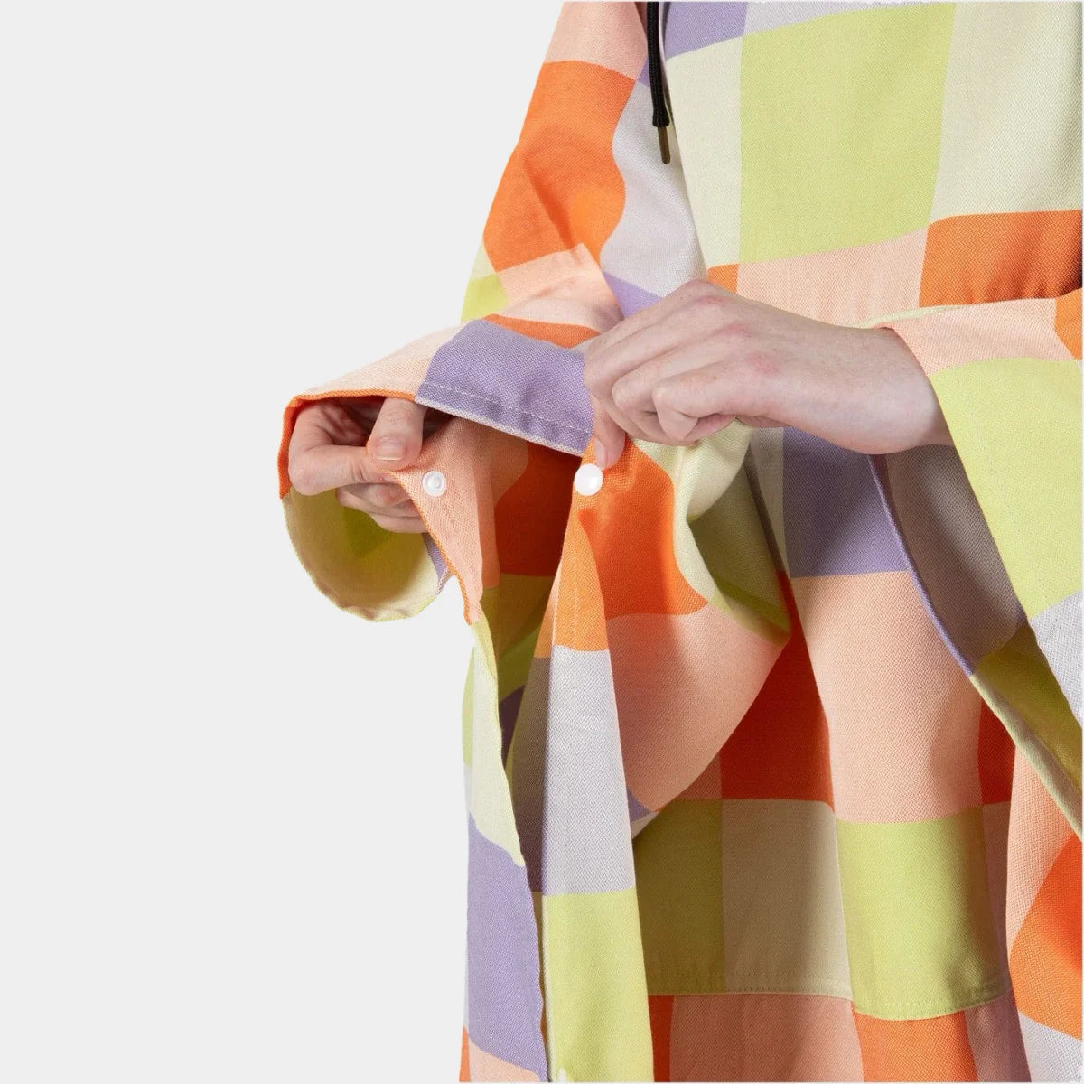 Person wrapped in colorful block patterned oversized poncho blanket in orange, yellow, purple, and cream tones