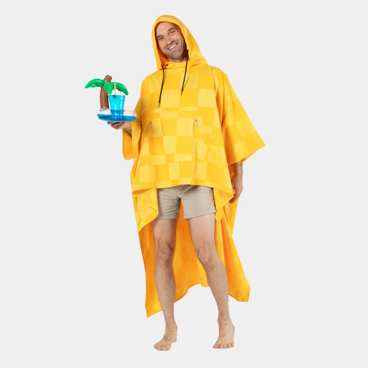 Man wearing golden checkered oversized poncho blanket with hood, holding tropical drink