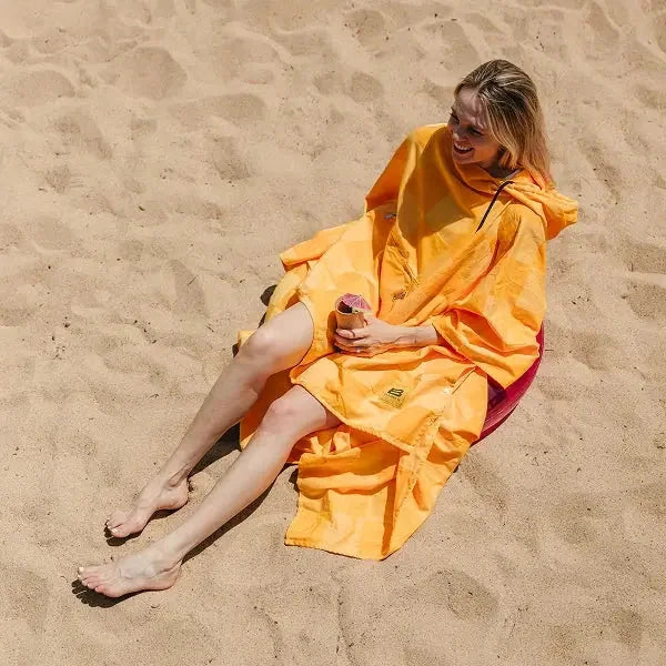 Woman wearing golden yellow oversized poncho relaxing on beach sand