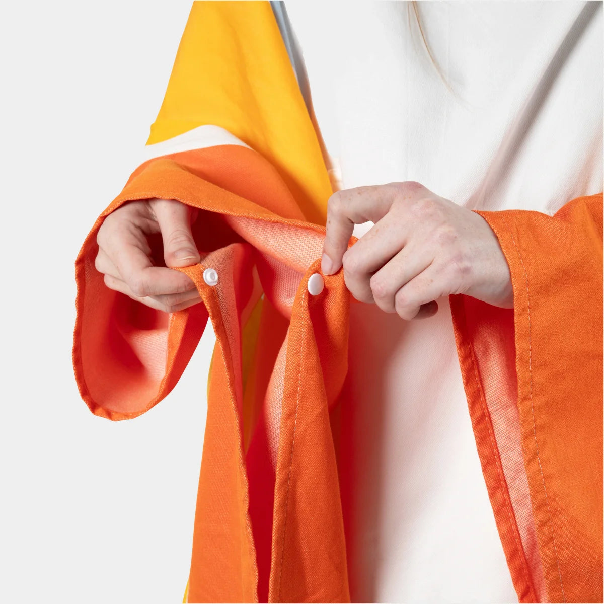 Child holding Big Beachy Poncho in sunrise stripes with orange, yellow, and white color-blocked design and snap closures