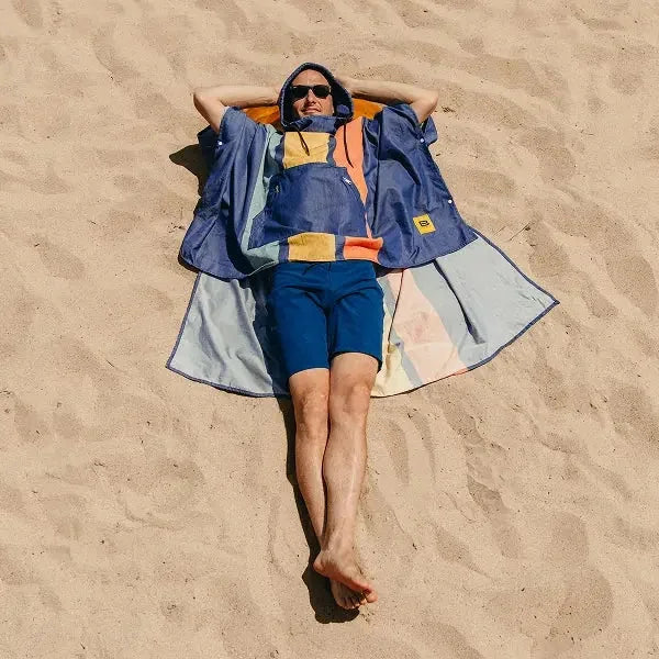 Person lying on sand wearing navy and orange striped oversized beach poncho blanket