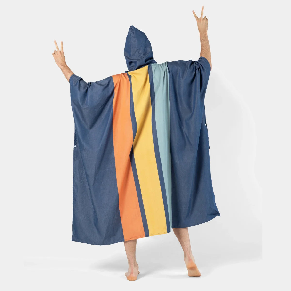 Person wearing navy oversized poncho blanket with orange, yellow, and blue stripe center panel, hood up, arms raised celebratory