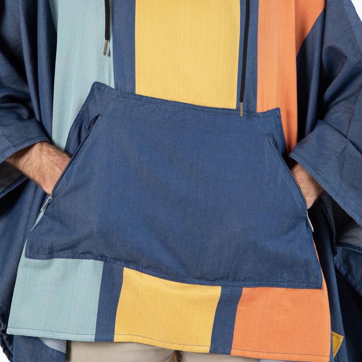 Navy, yellow, and orange striped oversized poncho with color-block design held by person wearing neutral pants