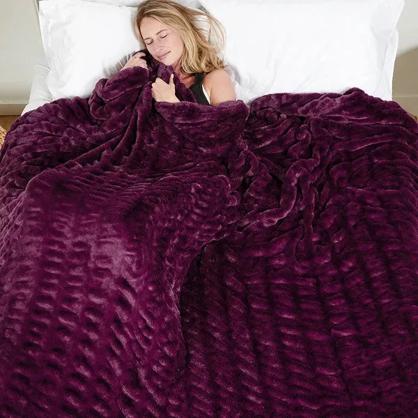 Woman snuggled in plum velvet Cloud Luxe oversized blanket on bed with white pillows