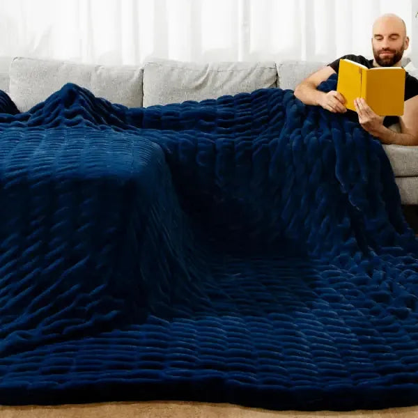 Man reading on couch under oversized navy blue textured blanket draped across seating area