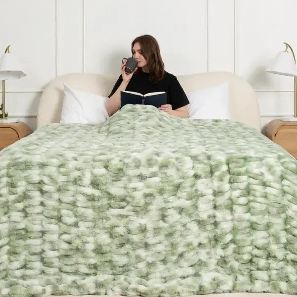 Woman reading in bed covered with sage green and white cloud-textured oversized blanket