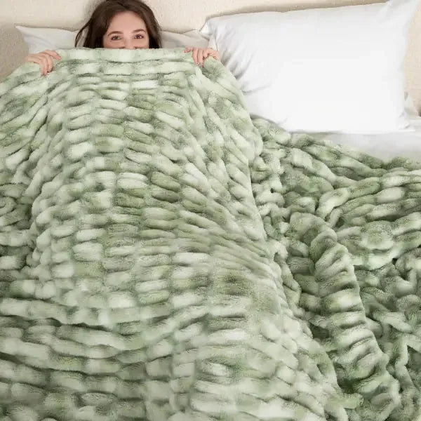 Woman wrapped in oversized sage green textured blanket on bed, showing plush ribbed fabric detail