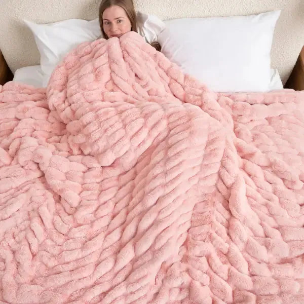 Woman snuggled under rose pink textured oversized blanket on bed with white pillows