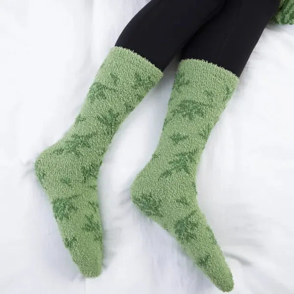 Pair of soft green fuzzy socks with black cuff displayed on white oversized blanket