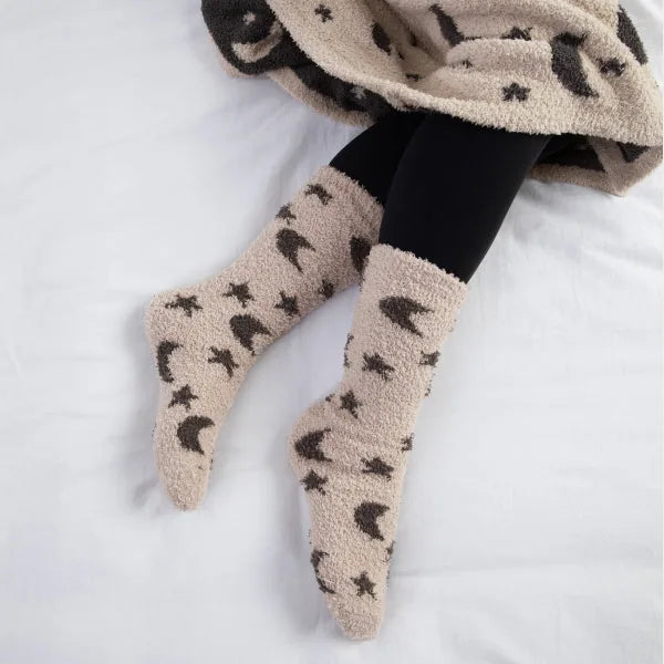 Cream and black star-patterned cozy socks on legs draped over oversized blanket