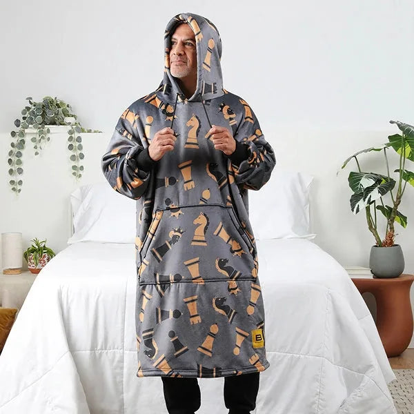 Person wearing gray hoodie blanket with chess piece pattern, standing on bed with white comforter