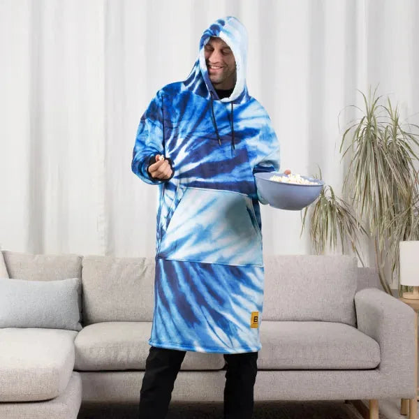 Blue tie-dye Hideout Hoodie with kangaroo pocket worn by person standing in living room holding snack bowl