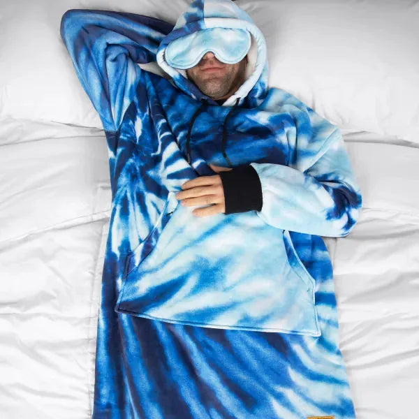 Person wrapped in blue tie-dye oversized blanket with hood and eye mask, lying on white bedding