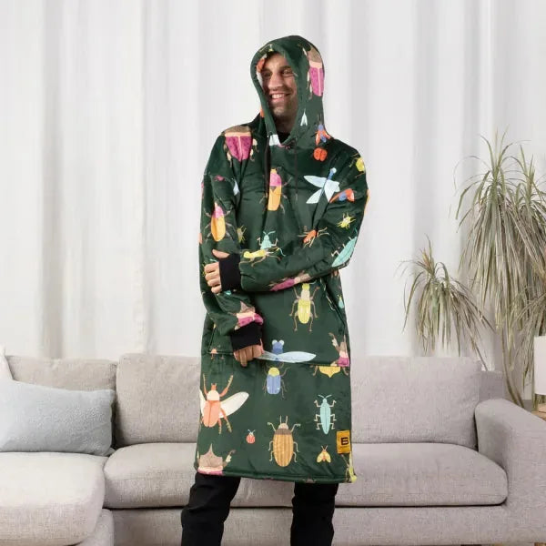 Person wearing dark green Hideout Hoodie with colorful insect print, hood up, standing in front of gray couch
