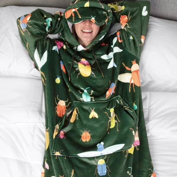 Person wrapped in green Hideout Hoodie with colorful bug print, lying on white bedding, wearing matching eye mask