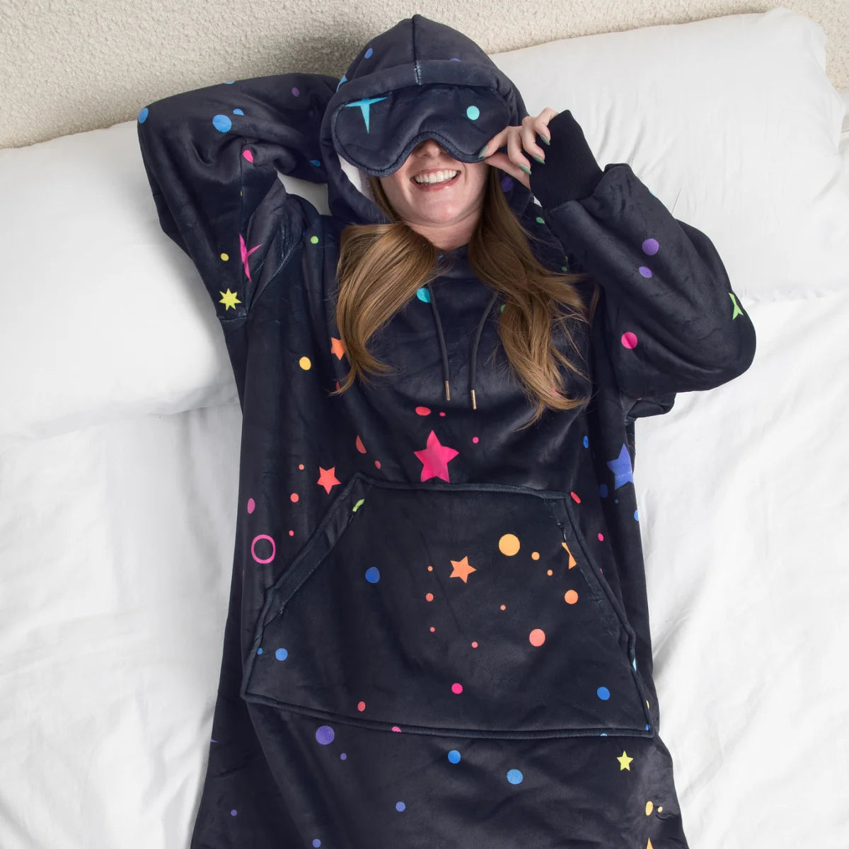 Person lying in bed in the Electric Sky Hideout Hoodie™ with the built-in eye mask pulled down