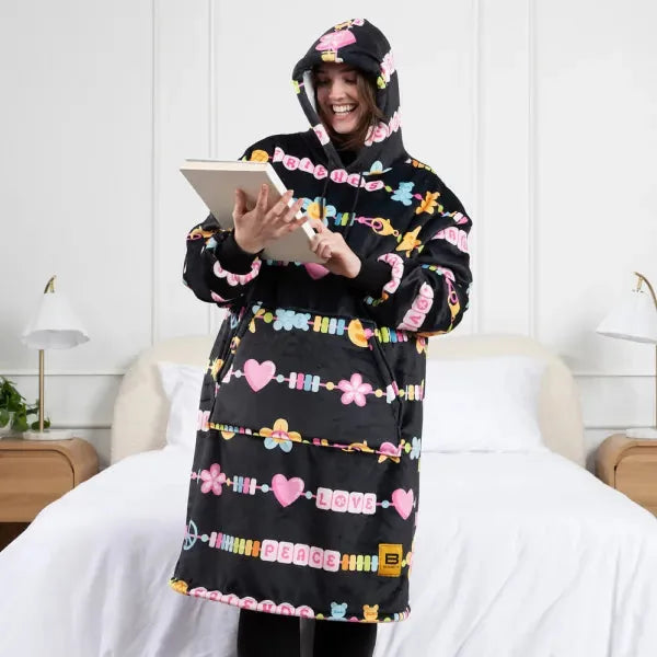 Person wearing black Hideout Hoodie with colorful candy and word print, holding tablet on bed