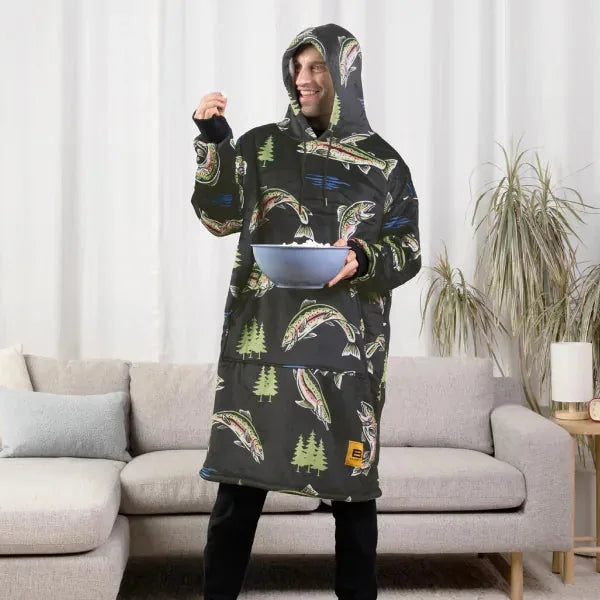 Person wearing black Hideout Hoodie with taco and pine tree print, holding bowl, standing in front of gray couch