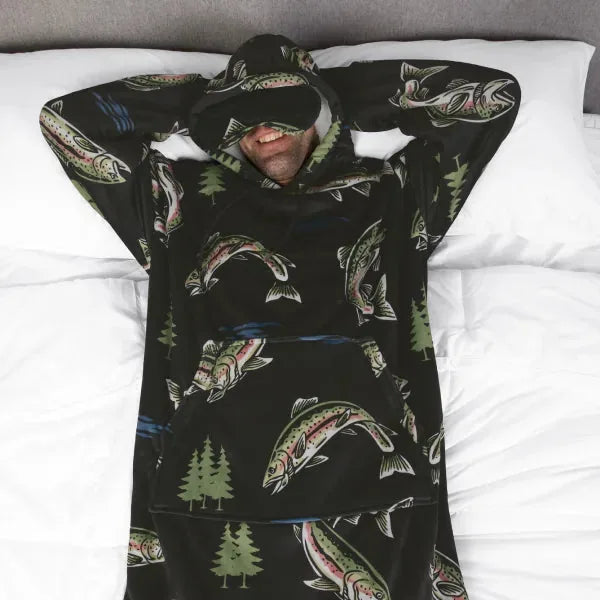 Black oversized hoodie blanket with fish and tree pattern, person relaxing on bed with hood up