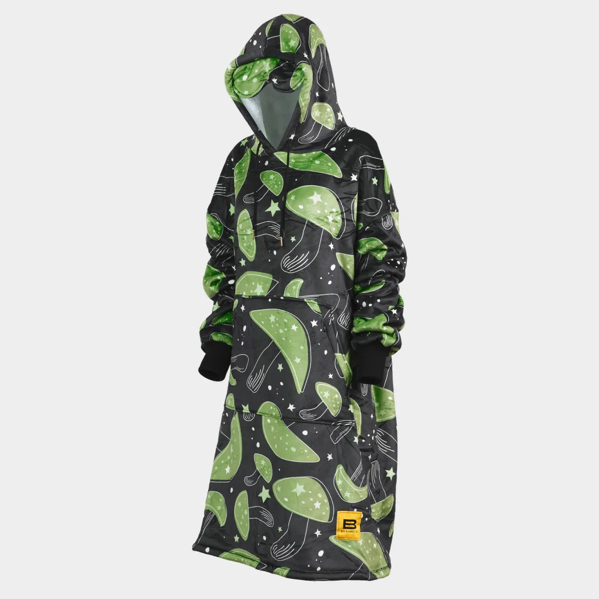 Hideout Hoodie™ wearable blanket in Mystic Mushrooms, side view with the hood up and the built-in eye mask on the hood — near-black charcoal ground scattered with large green mushroom caps, cream stars and speckles