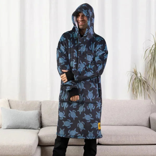 Man wearing navy blue Hideout Hoodie with blue turtle pattern, standing on couch with hood up