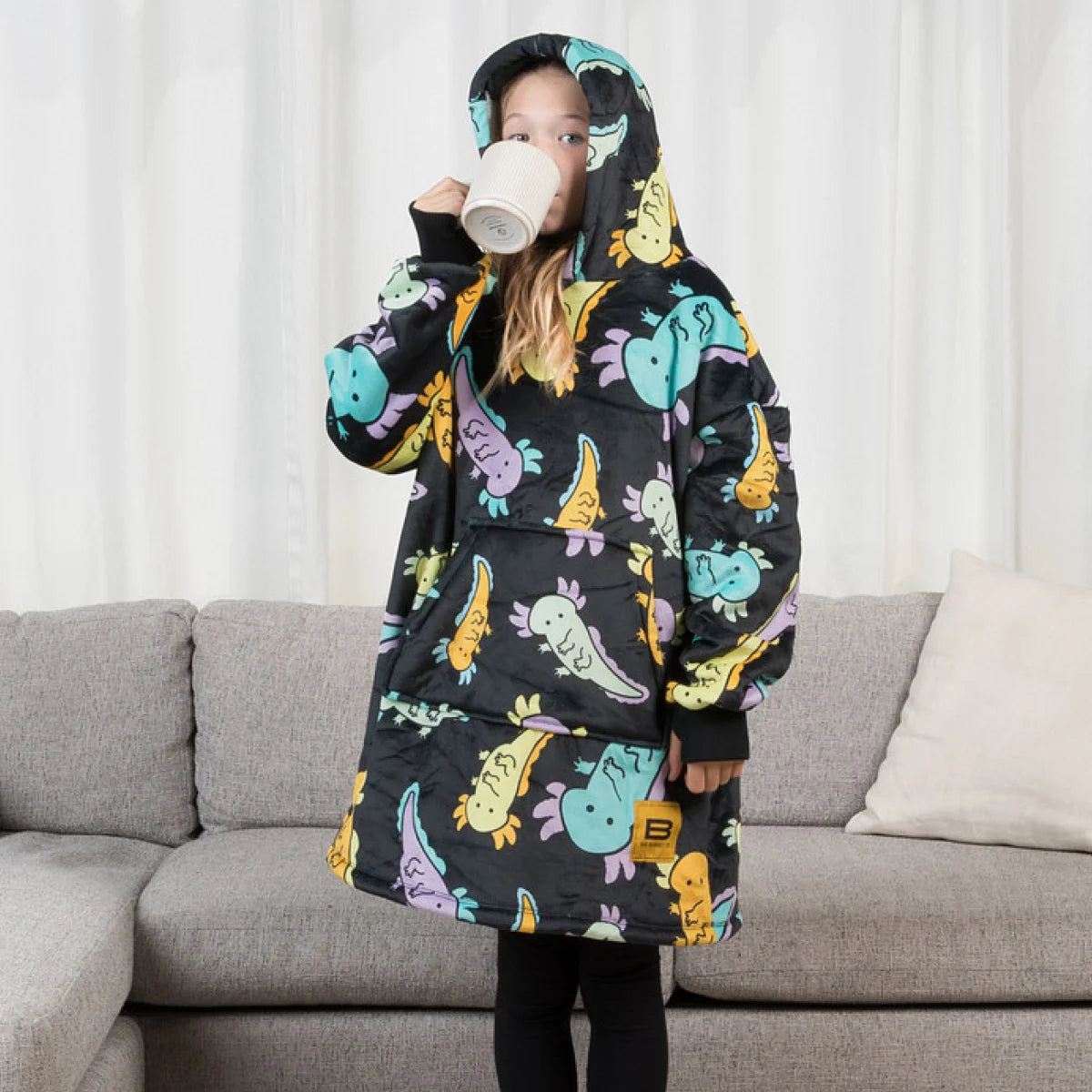 Child drinking from a mug while wearing the Axolotl Drift Hideout Hoodie™ Kids wearable blanket