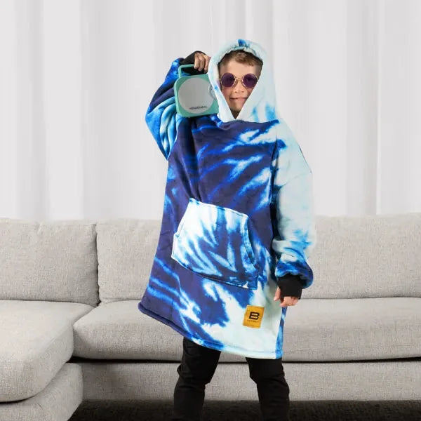Person wearing blue tie-dye oversized Hideout Hoodie with kangaroo pocket, holding hood closed with sunglasses on indoors