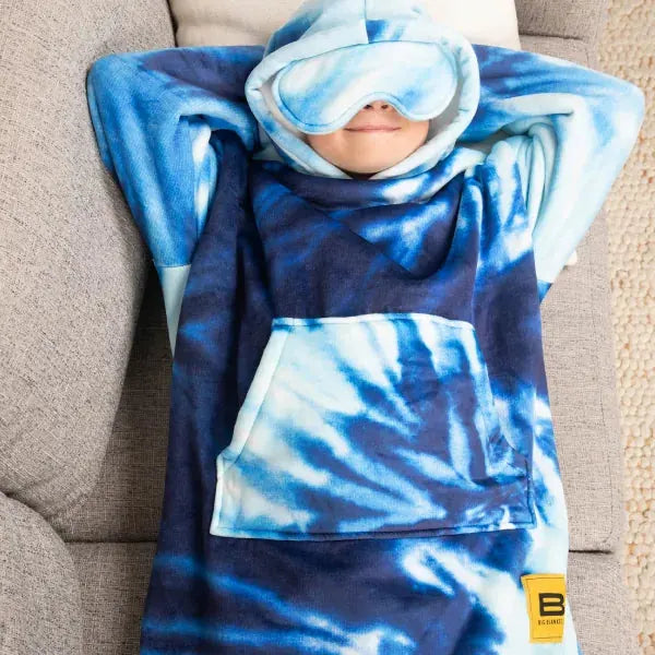 Child wrapped in blue tie-dye oversized blanket with attached hood and eye mask on gray couch