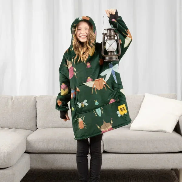 Child wearing forest green Hideout Hoodie with camping print, holding lantern while standing on couch