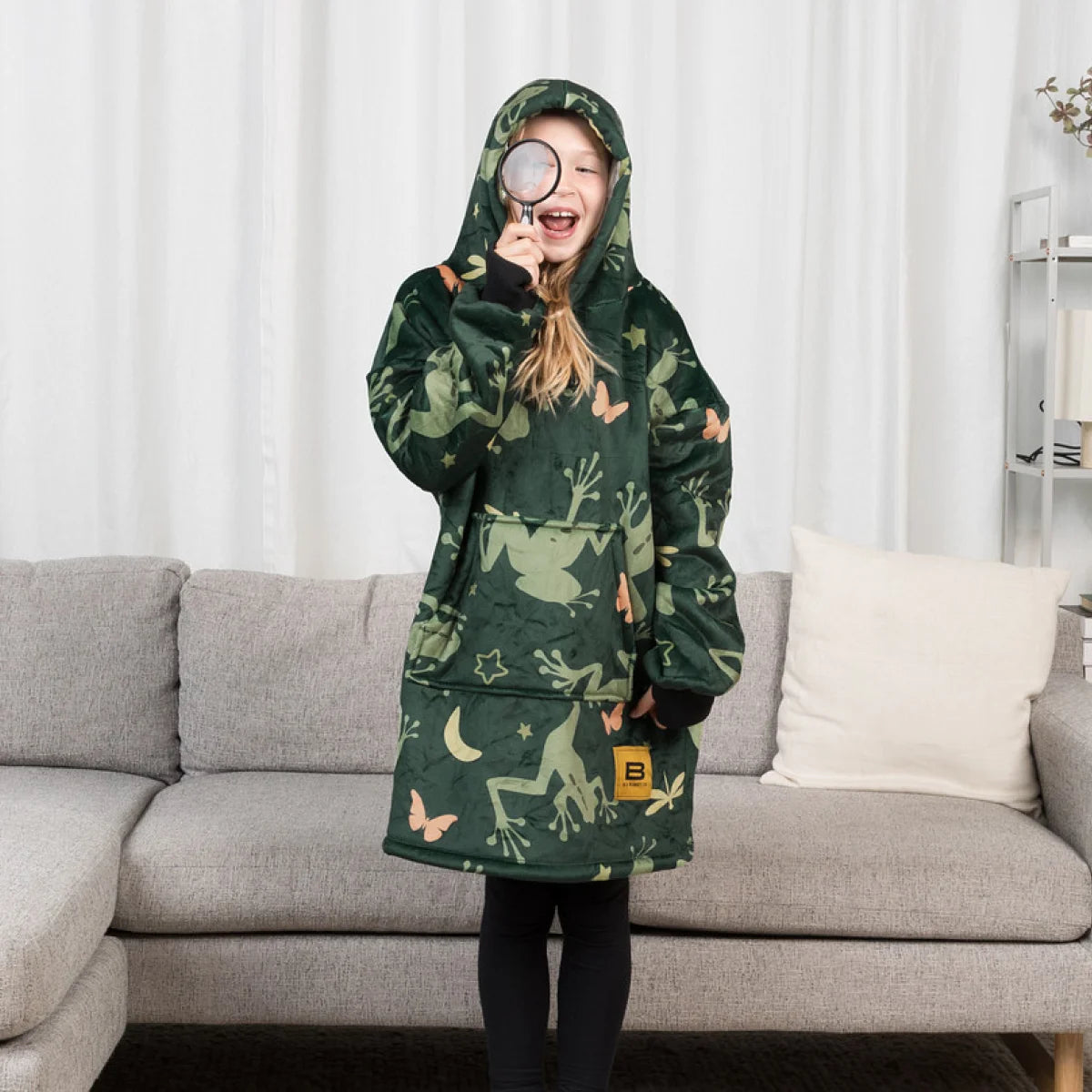 Child drinking from a mug while wearing the Dreamy Frogs Hideout Hoodie™ Kids wearable blanket