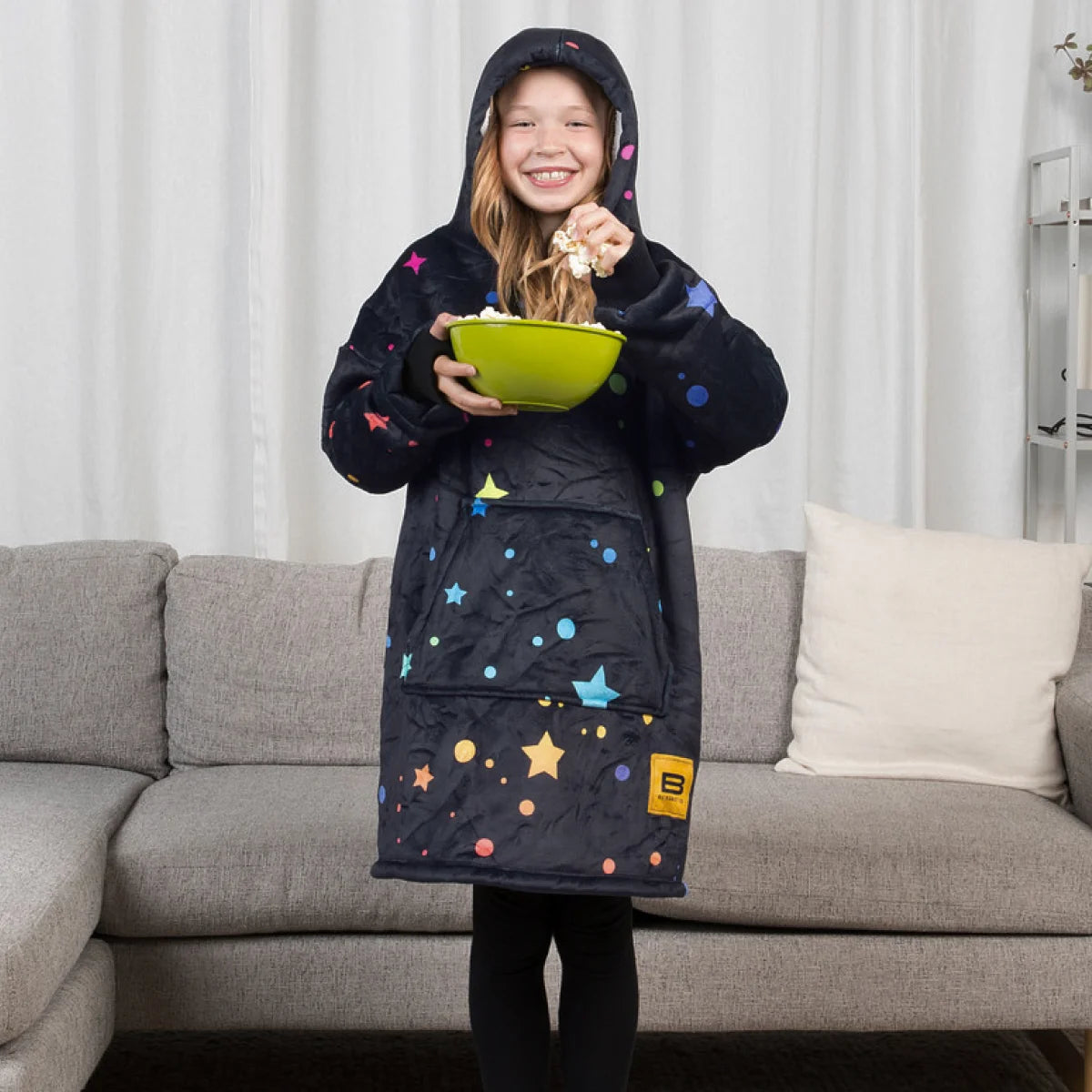 Child holding a bowl of popcorn while wearing the Electric Sky Hideout Hoodie™ Kids with the hood up