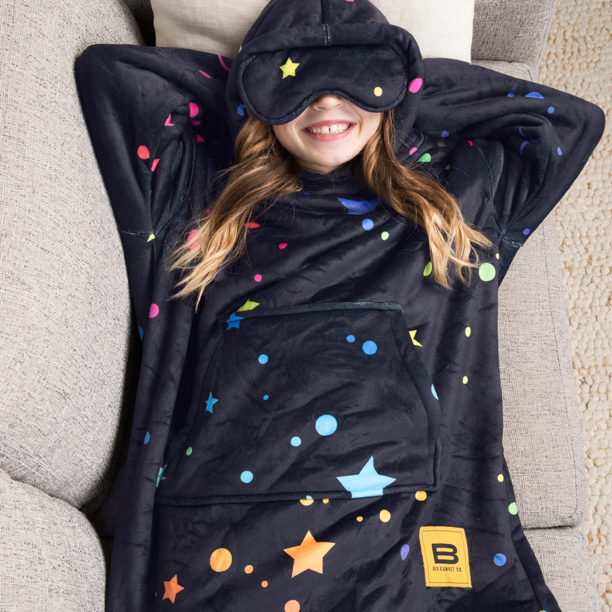 Child lying back on a couch in the Electric Sky Hideout Hoodie™ Kids with the eye mask pulled down