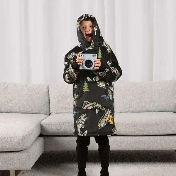 Child wearing black Hideout Hoodie with feather and tree print, standing in front of gray sectional couch