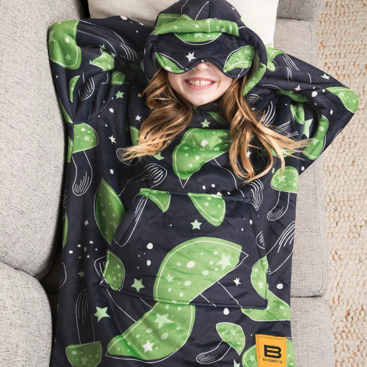 Child lying back on a couch in the Mystic Mushrooms Hideout Hoodie™ Kids with the built-in eye mask pulled down