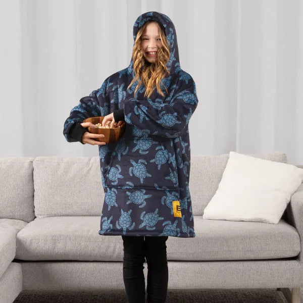 Child wearing navy Hideout Hoodie with turtle pattern and hood, standing on beige sofa with white pillow