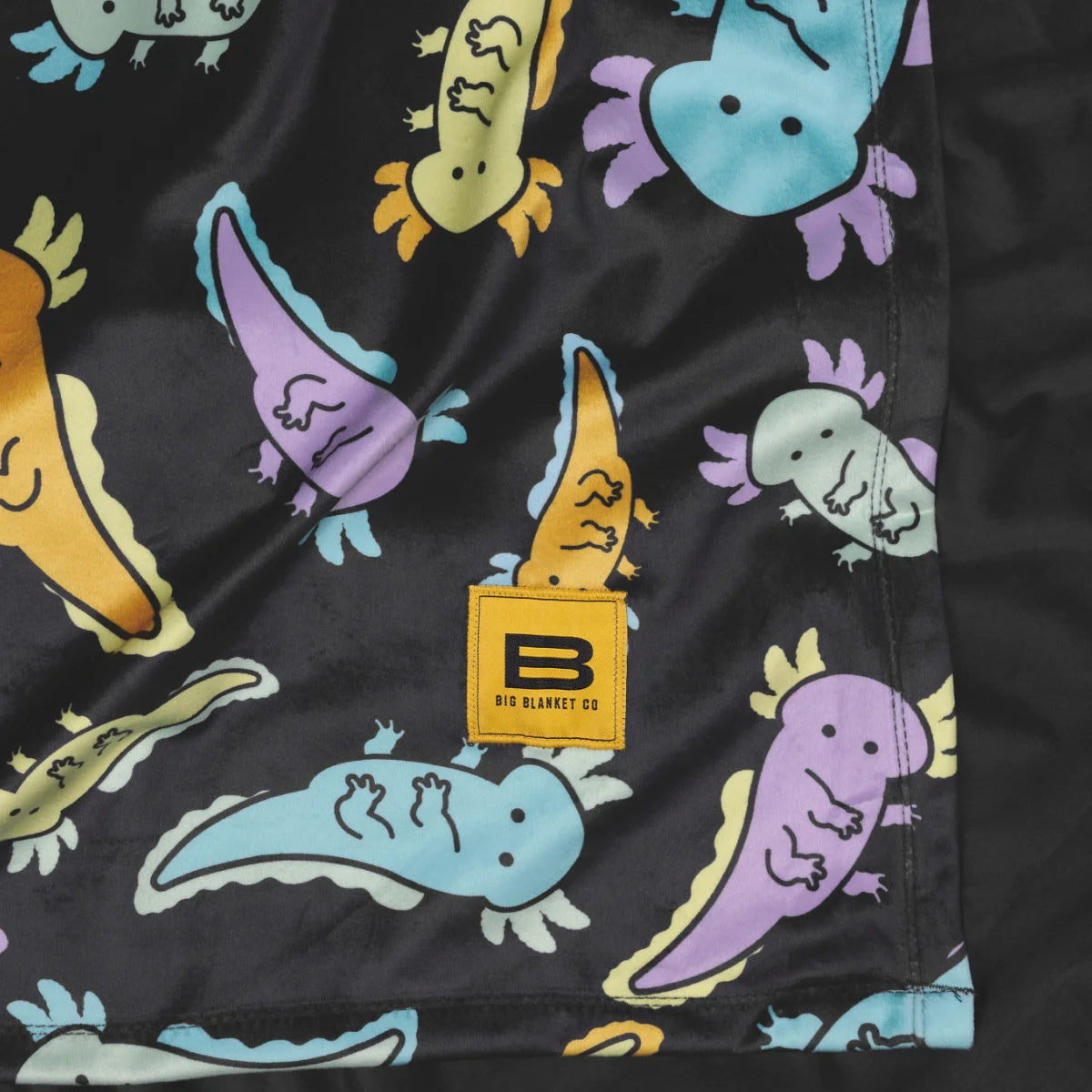 Close-up of the Axolotl Drift Original Stretch™ blanket showing the print and the yellow Big Blanket Co label