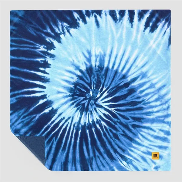 Blue tie-dye oversized blanket with radial starburst pattern, corner folded to show solid navy reverse side