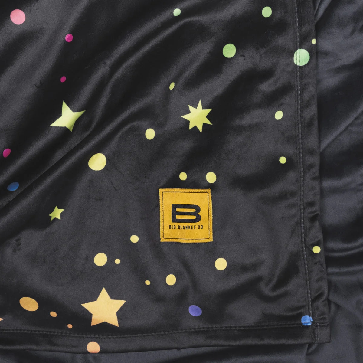Close-up of the Electric Sky Original Stretch™ blanket showing the multicolour star print and the yellow Big Blanket Co label
