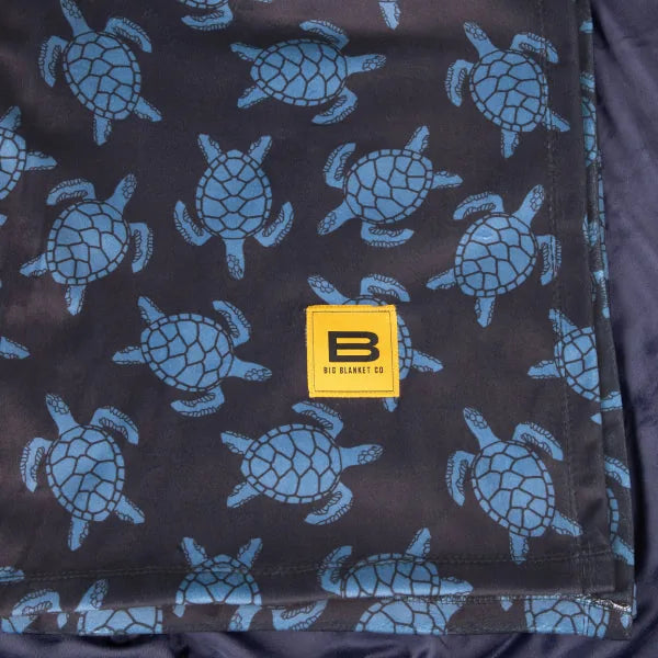Charcoal blanket with repeating blue sea turtle pattern and Big Blanket Co yellow logo label