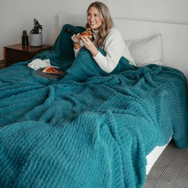 Woman wrapped in teal oversized blanket eating pizza on bed, showing texture and coverage of Premier Plush Blanket