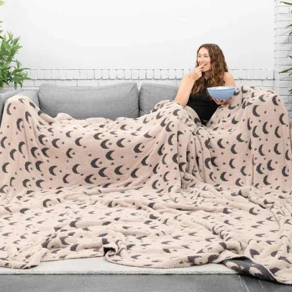 Woman relaxing on couch wrapped in cream oversized blanket with moon print pattern