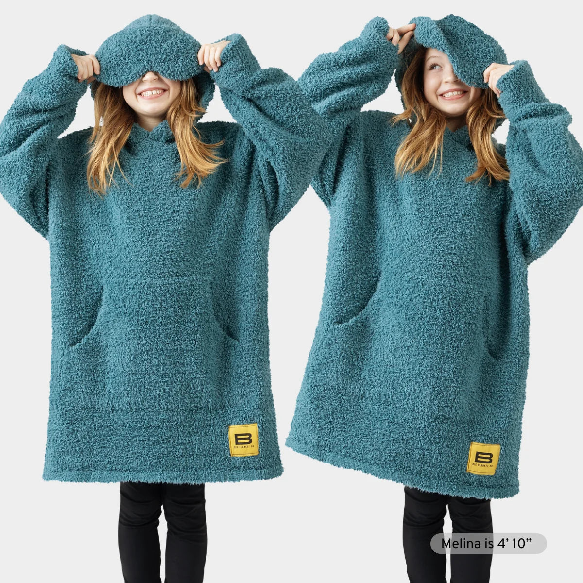 Child wearing oversized teal textured hoodie blanket with kangaroo pocket, pulling hood over eyes playfully